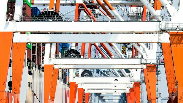 A row of working gantry cranes and shipping containers at a port.