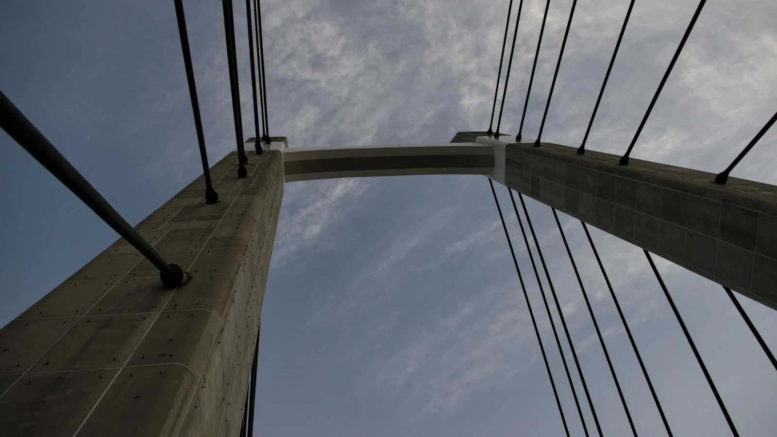 Concrete towers and suspension cables carrying the load of a bridge, viewed from below.
